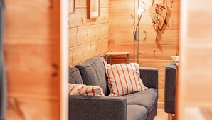 Een gezellige kamer met een grijze bank, gestreepte kussens, een kleine tafel en een houten wand.