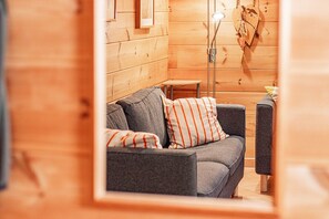A cozy room with a grey sofa, striped pillows, a small table, and a wooden wall.