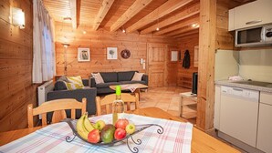 Een gezellig houten blokhut interieur met een eethoek, een bank, een keuken met een magnetron en een televisie.