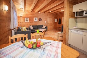 A cozy wooden cabin interior with a dining area, a sofa, a kitchen with a microwave, and a television.