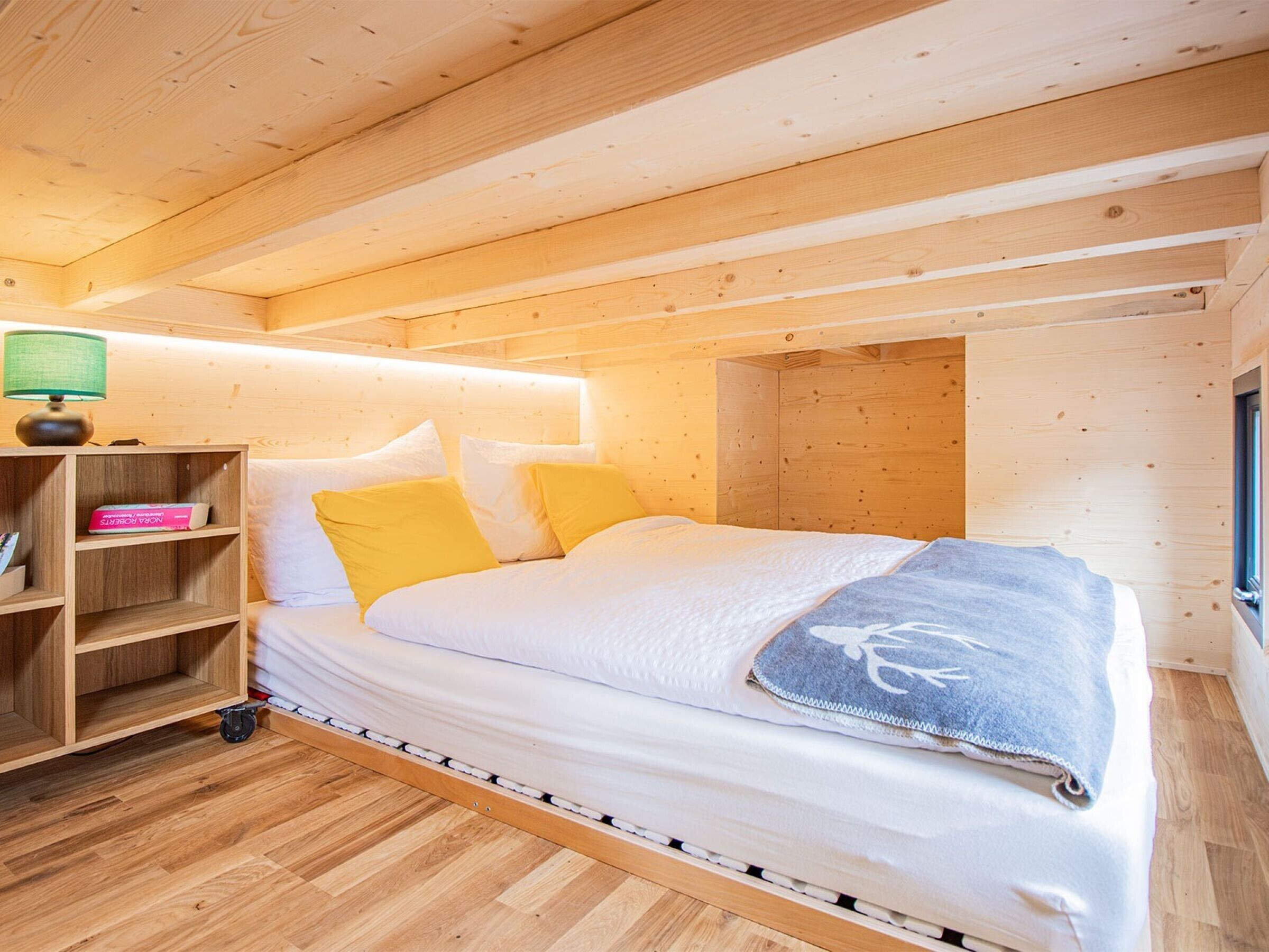 Dormitorio de cabaña de madera con una cama, una mesita de noche, una lámpara y una ventana.