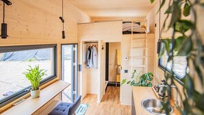 Ein gemütlicher, kleiner Innenraum aus Holz mit einer Küchenzeile, einer Bank, einer Pflanze und Blick durch ein Fenster.