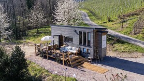 Ein modernes Blockhaus mit einer Terrasse, einer kleinen Veranda und Blick auf einen Weinberg.