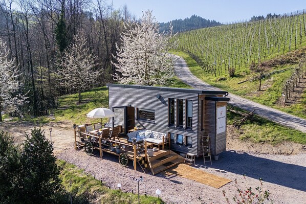 A modern cabin with a patio area, a small deck, and a view of a vineyard.