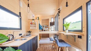 Eine kompakte, moderne Küche mit Holzwänden, einem Essbereich und einem großen Fenster mit Blick auf eine grüne Landschaft.