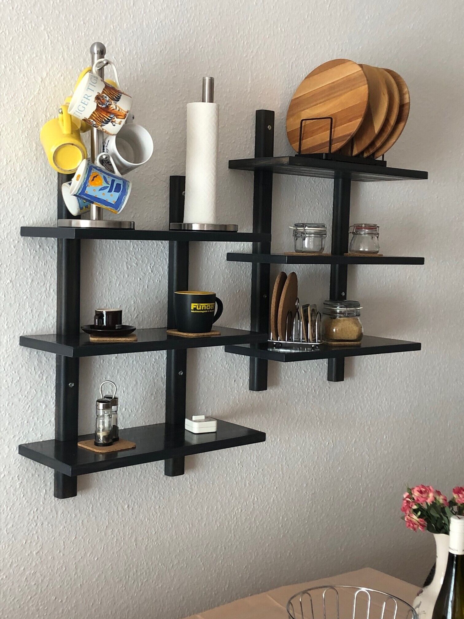 A black metal shelf unit with various kitchen items including a kettle, mug, and wooden plates.