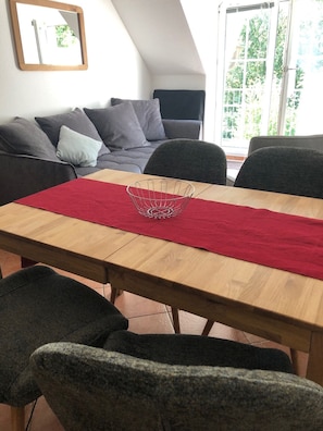 Un coin repas avec une table en bois, un chemin de table rouge et des chaises grises.