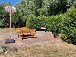 A patio area with a basketball hoop, wooden benches, a barbecue grill, and a green chair.