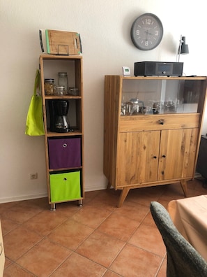 Une pièce avec un meuble en bois, une étagère remplie de bocaux, un sac vert et une horloge au mur.