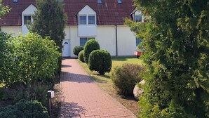 En bygning med to etager, rødt tegltag, hvide facader og en belagt indkørsel, der fører til en hvid dør.