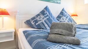 Una cama bien hecha con ropa de cama azul, dos almohadas con un estampado de notas musicales, una toalla doblada y un cuadro en la pared.