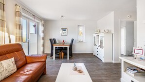 Una sala de estar con un sofá de cuero, una mesa de comedor con sillas, una mesa de centro blanca y un mueble blanco con cajones.