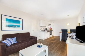 Ein modernes Wohnzimmer mit einem braunen Sofa, einem weißen Couchtisch und einer Küchenzeile mit weißen Schränken sowie einer schwarzen TV-Konsole.