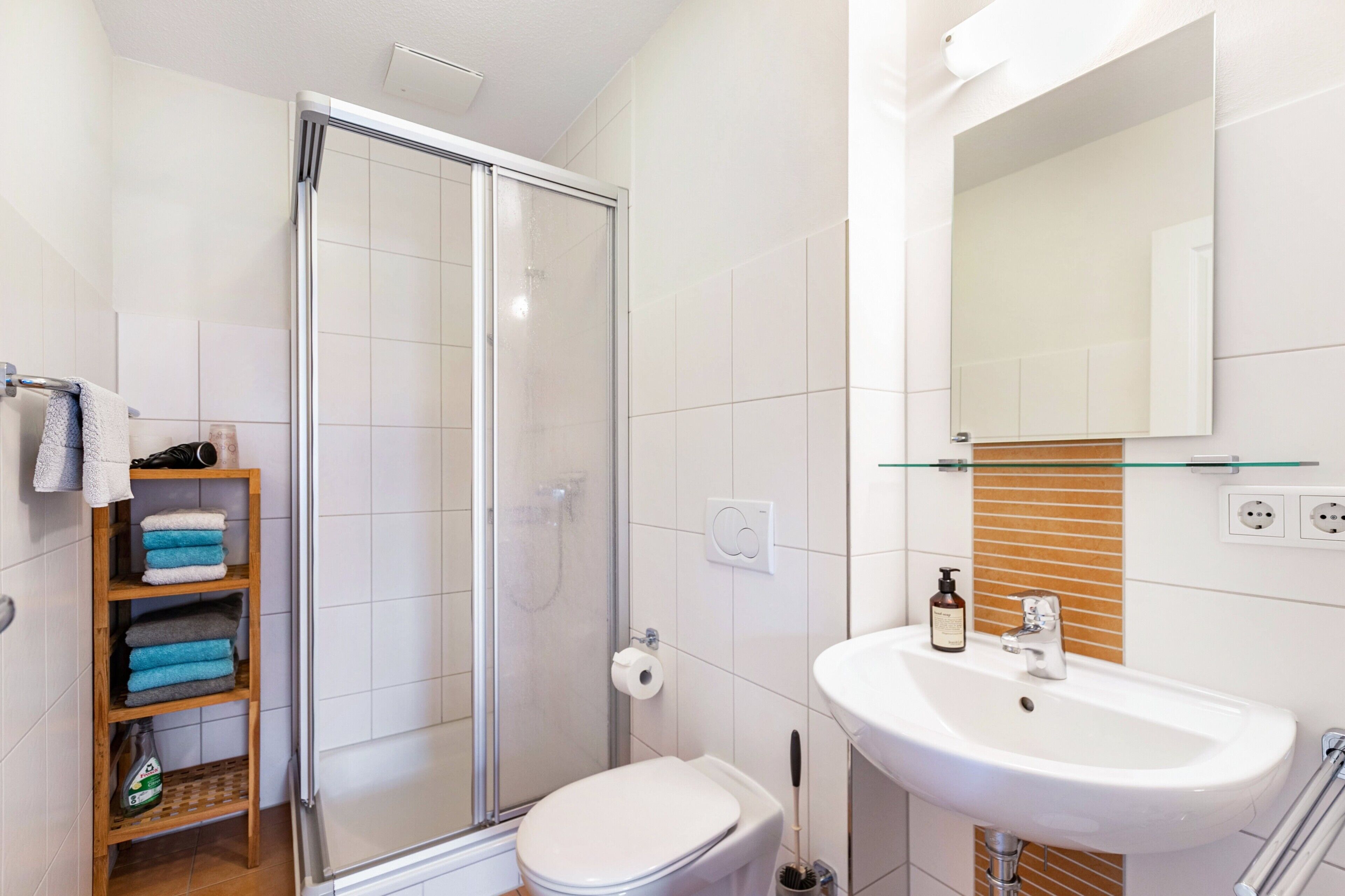 Een badkamer met een douchecabine van glas, een witte wastafel, een toilet en een plank met handdoeken.