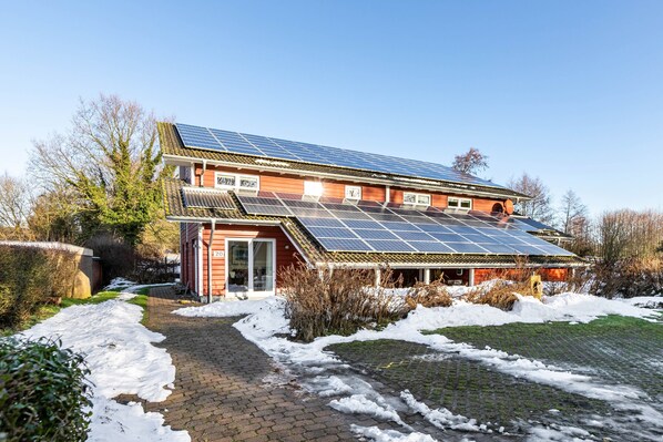 Ein Gebäude mit Solaranlage auf dem Dach, einem Ziegelweg und Schnee auf dem Gelände.