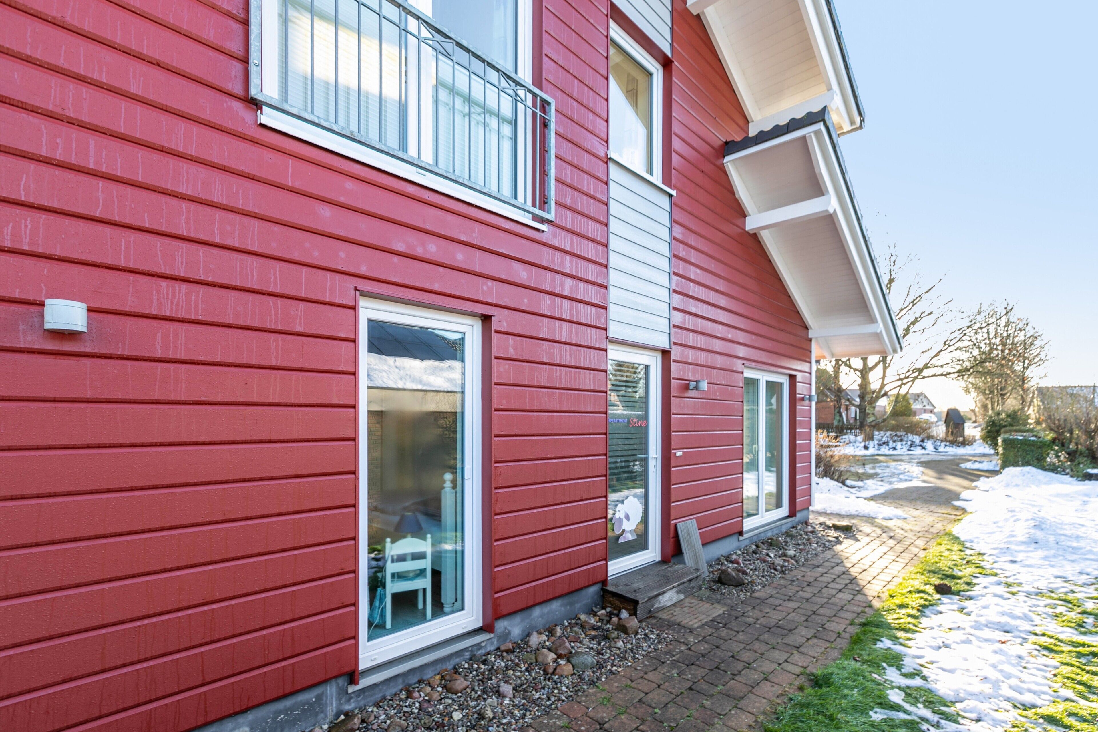 A red two-story house with a visible window, a door, and a small porch area.