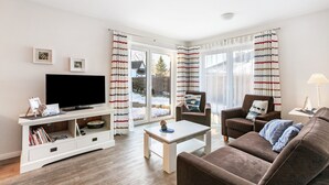 A living room with a flat-screen TV, a sofa, a coffee table, and a television stand with books. - Apartment 'Stine' with Shared Terrace, Shared Garden and Wi-Fi (Breklum)