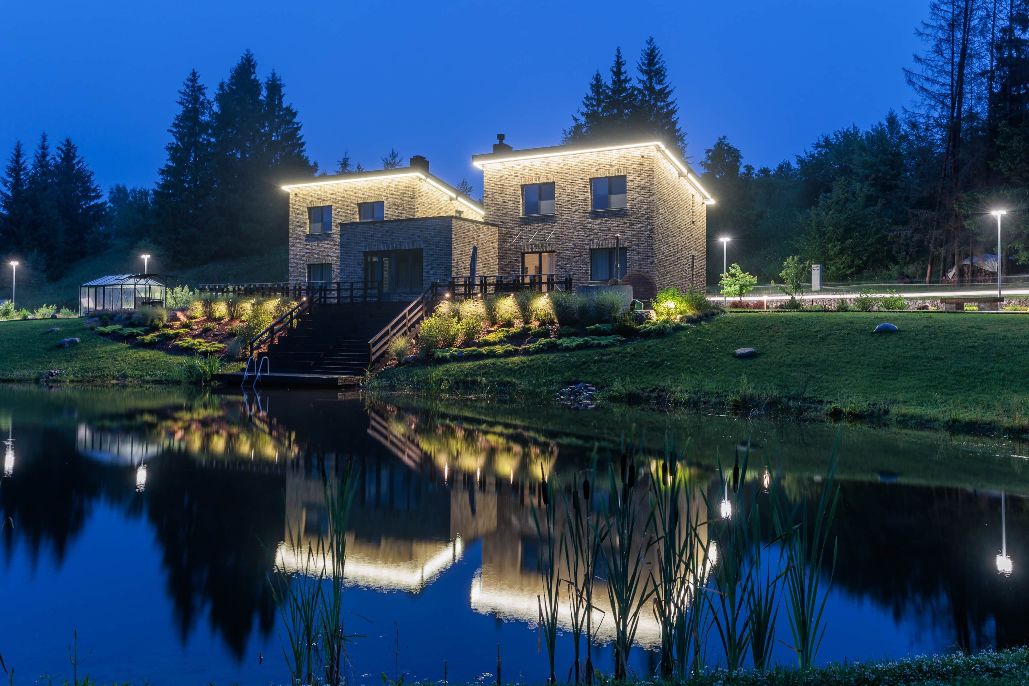 A two-story building with a reflective pond in front, surrounded by trees and a well-lit pathway.