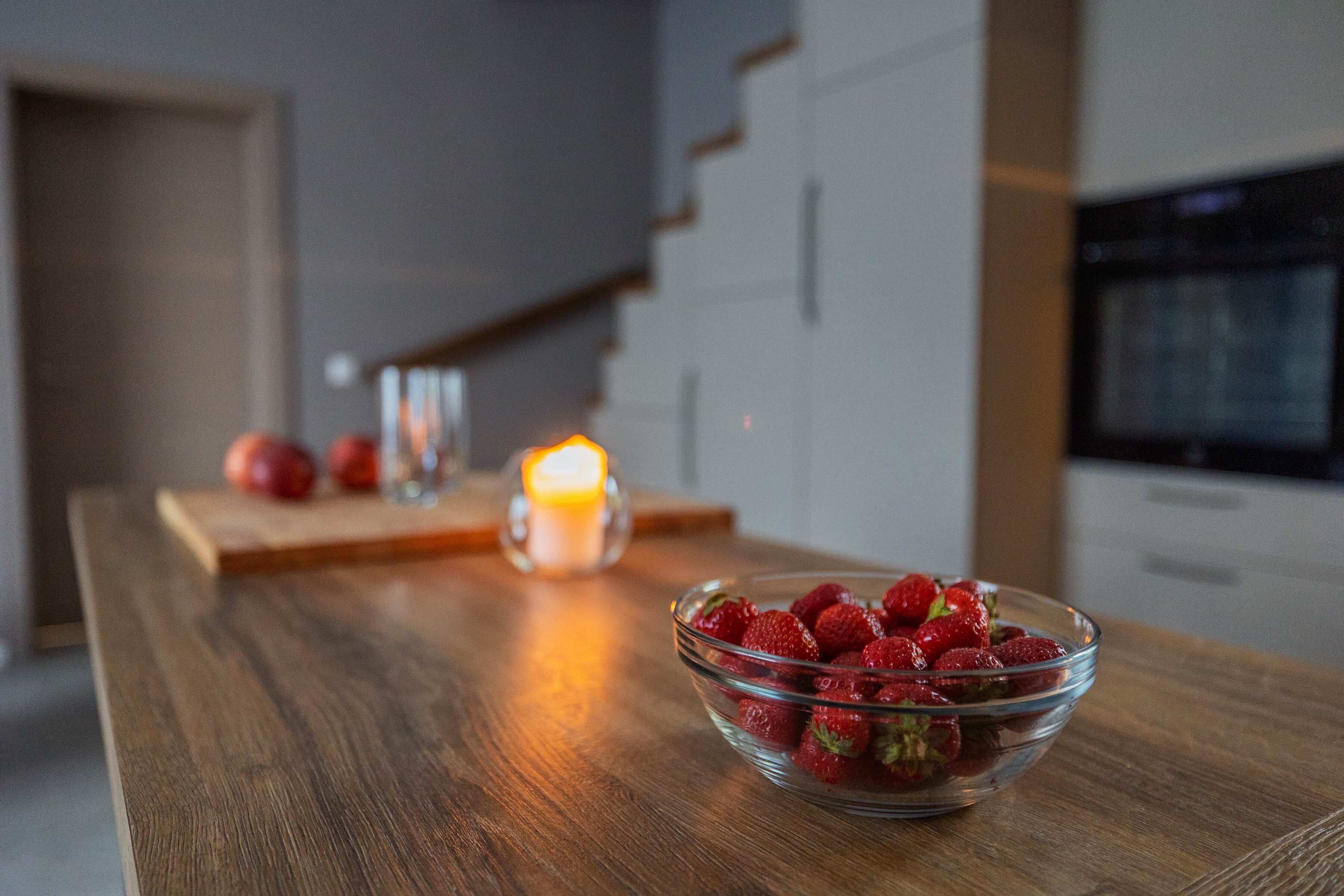 A wooden table with a glass bowl of strawberries, a lit candle, and a glass of water.