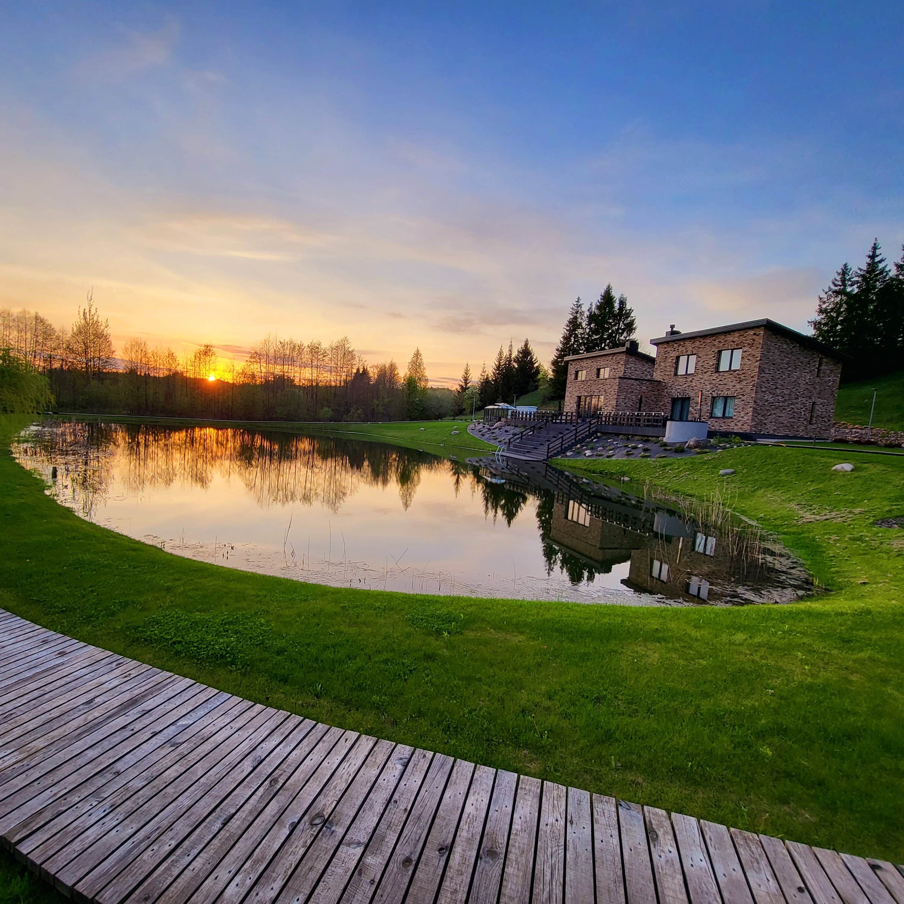 A lakeside property with a wooden deck, a stone building, and a reflection of the sunset in the water.