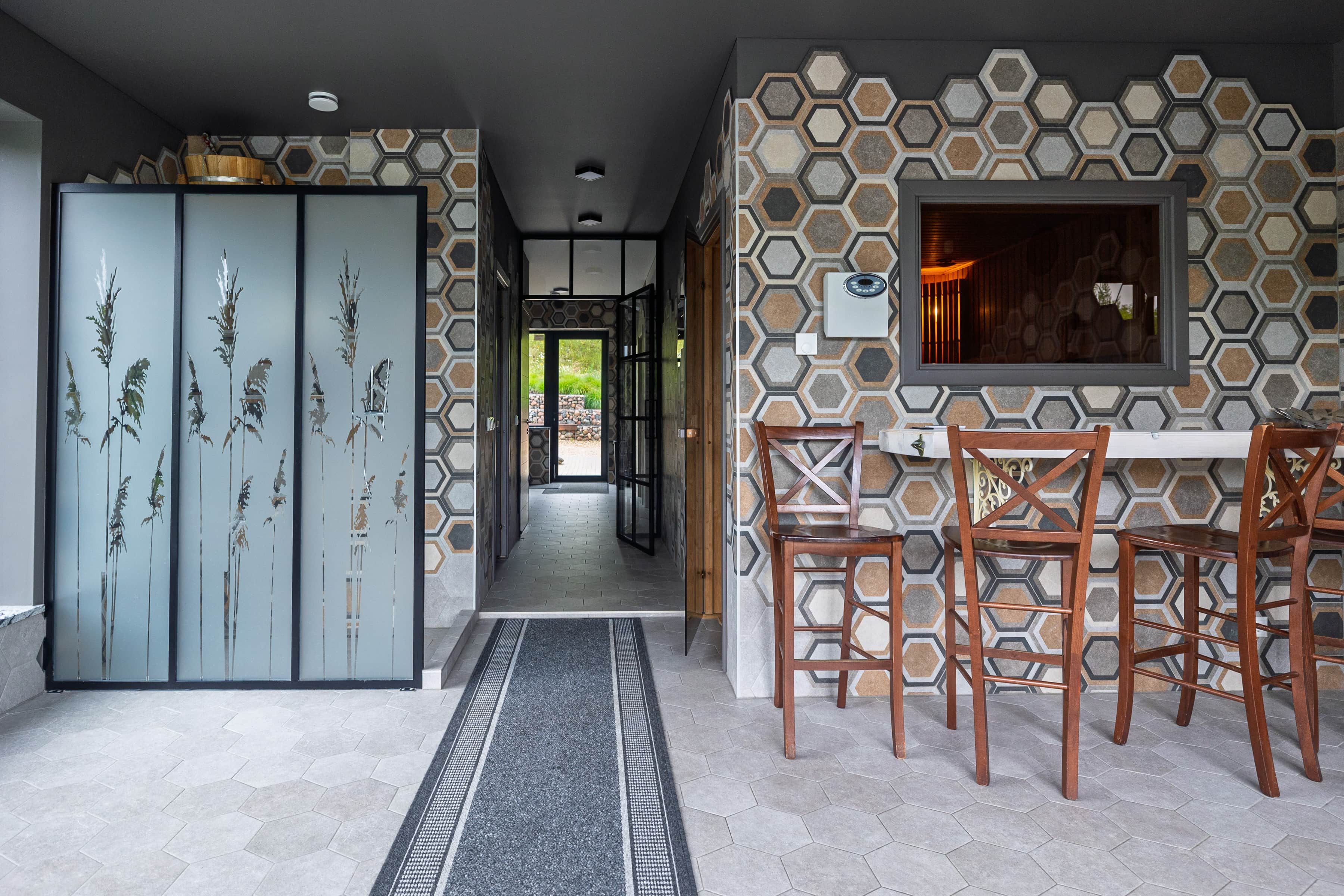A hallway with a patterned wall, a door with a glass panel, and a dining area with chairs and a table.