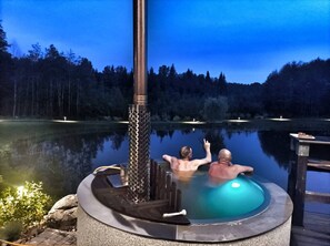 A hot tub with a chimney, surrounded by a calm lake and forested hills. - Lakeside Family Getaway – Modern Home with Private Pond (Semeliškės Eldership)