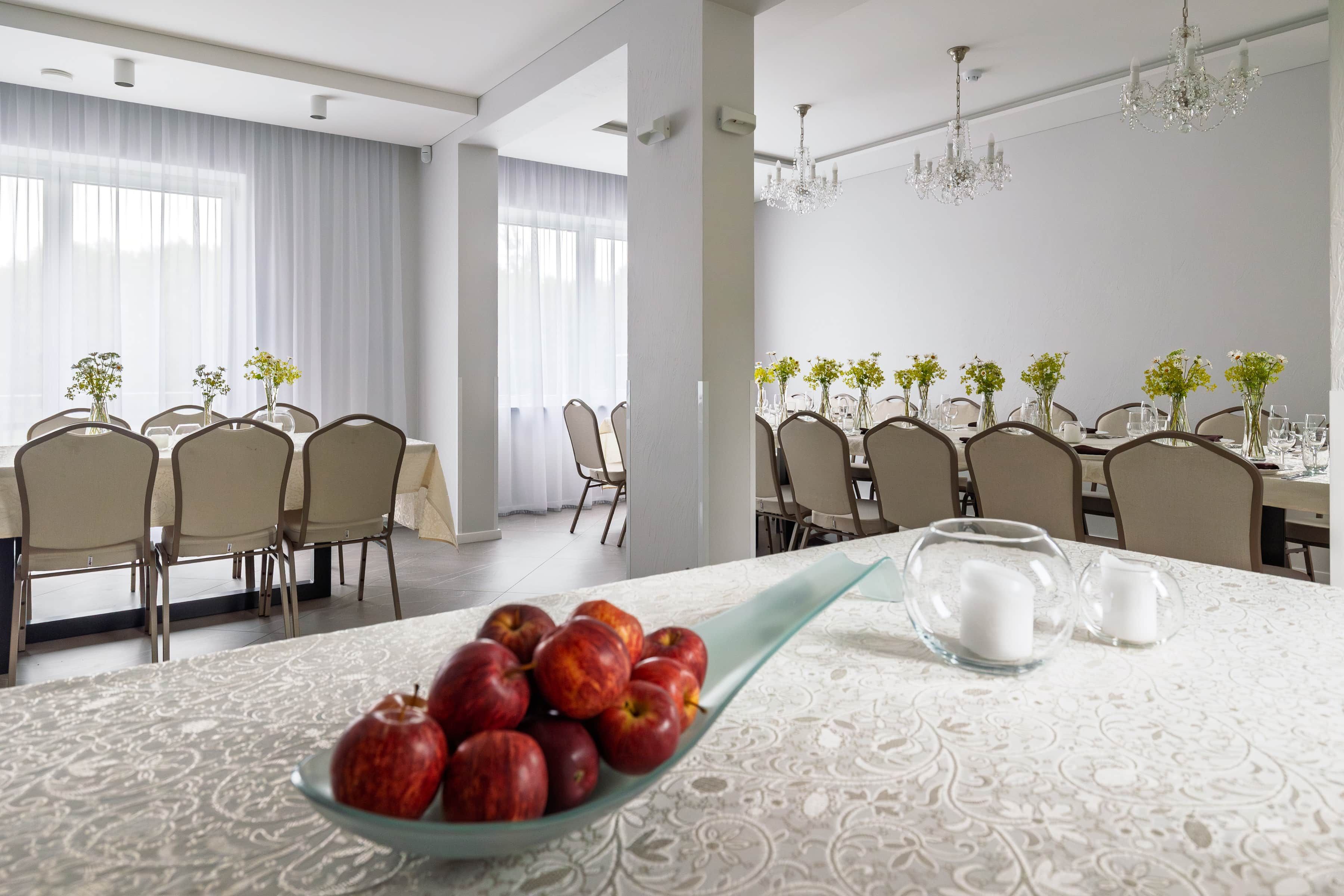Une salle à manger avec une longue table dressée pour un repas, agrémentée d’un saladier de pommes et d’une carafe d’eau.