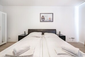 A double bed with white linens, a dark headboard, bedside tables with lamps, a framed artwork on the wall, and a white door. - Aldars Urban Suite No.5 with Wi-Fi and Air Conditioning (München)
