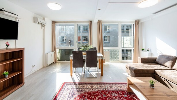 Una sala moderna con comedor, ventanas grandes y televisor de pantalla plana.