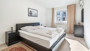 Una habitación de hotel moderna con cama, mesitas de noche, una ventana con cortinas y aire acondicionado de pared.