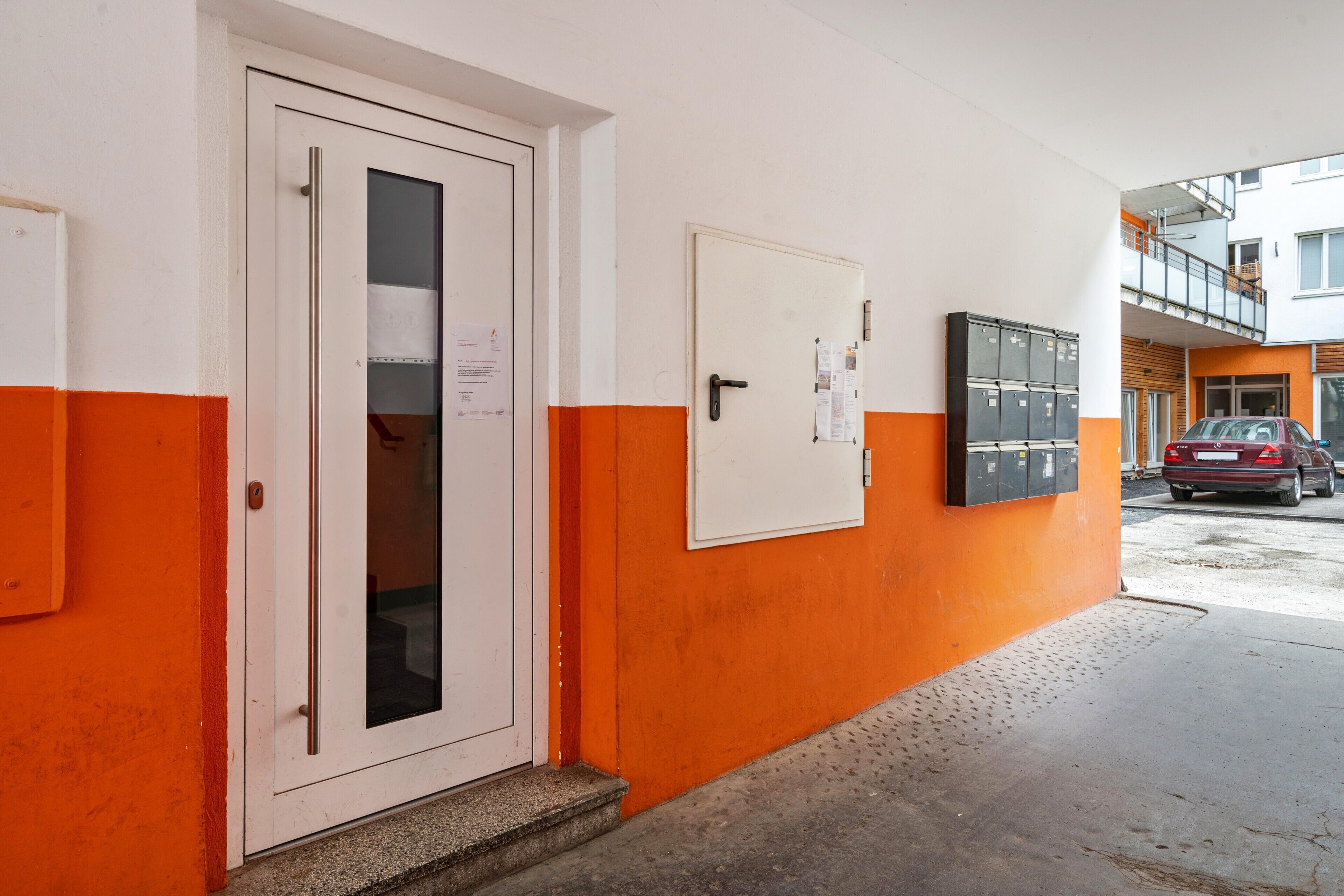 Um corredor com uma porta branca, um mural de avisos e uma fileira de armários.