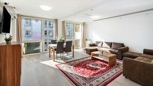 Amplia sala de estar con un conjunto de sofás, una mesa de comedor con sillas y un ventanal con vistas a edificios.