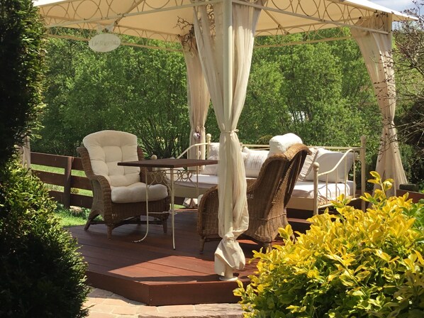 A gazebo with a table and chairs, surrounded by greenery.