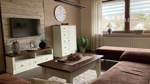 A living room with a flat-screen TV, a clock, a cabinet, a sofa, and a window with blinds.
