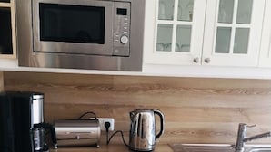 A kitchen with a stainless steel microwave, a coffee maker, a kettle, and a sink.