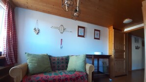 Un salon chaleureux avec un canapé à motifs, un plafond en bois et un coin repas comprenant une table et des chaises.