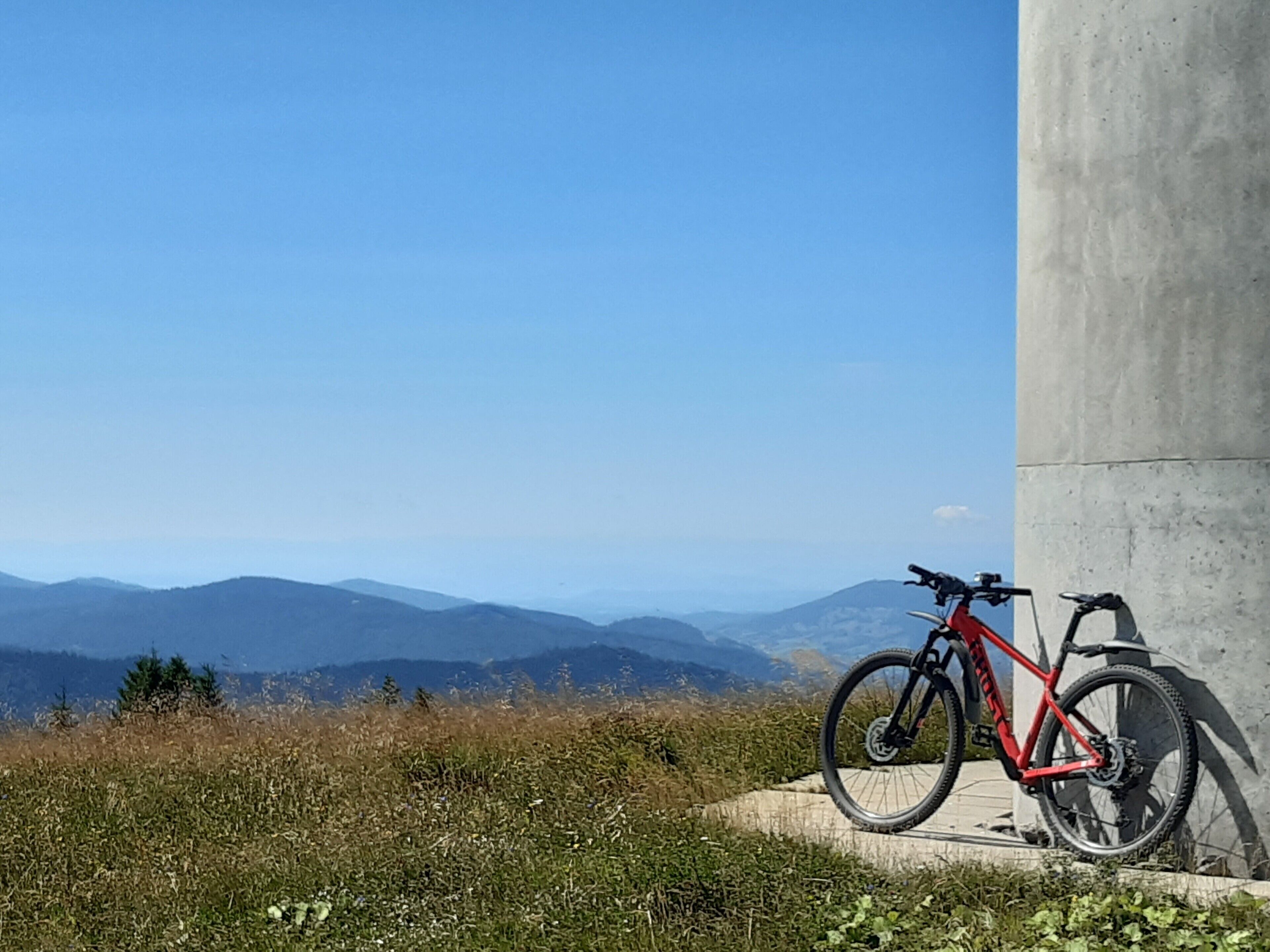 Un vélo est garé contre une structure en béton, avec une vue sur des montagnes lointaines.