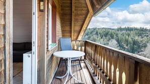 Un balcone in legno con un tavolo e una sedia, vista su una foresta e un muro in mattoni.