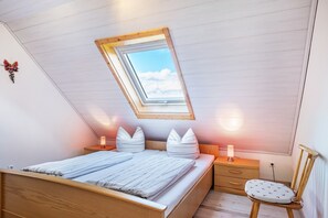 A bedroom with a skylight, a bed with pillows, bedside tables, a chair, and a dresser.