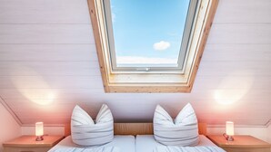 Una camera da letto con un lucernario, due comodini con lampade, un letto con lenzuola a righe e una testiera in legno.