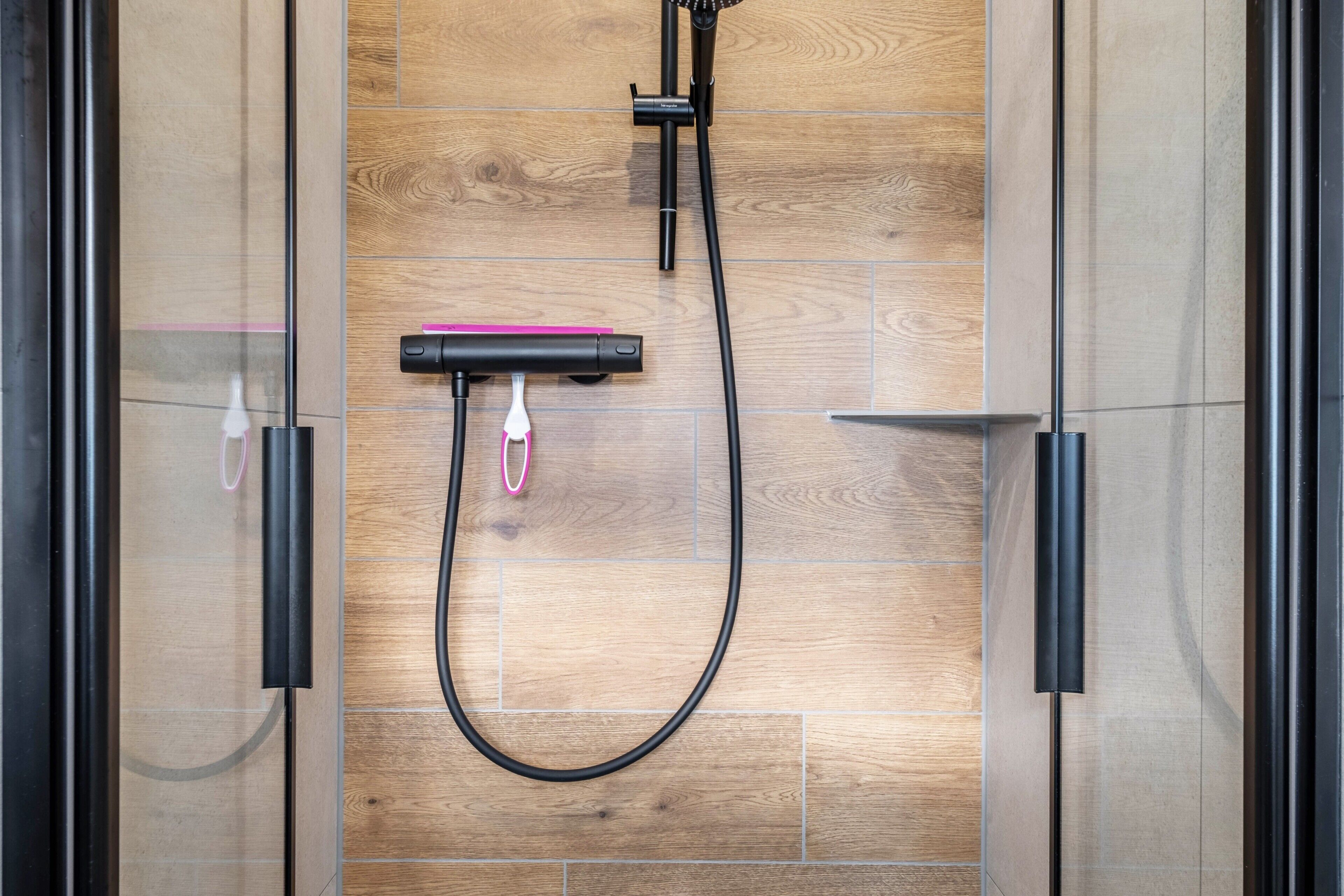 A shower with a handheld device, a hose, and a wall-mounted control panel.