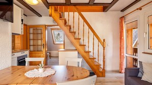 A wooden staircase leading to a loft bedroom, a dining area with a wooden table and chairs, and a living room with a sofa. - Apartment '2- Ost' with Private Garden, Balcony and Wi-Fi (Sankt Märgen)
