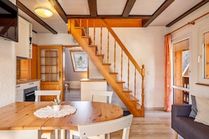 Un escalier en bois menant à une chambre aménagée en mezzanine, un coin repas avec une table et des chaises en bois, et un salon avec un canapé.