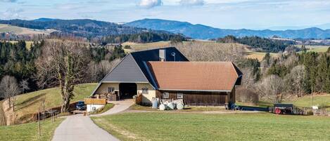 Una casa rural con entrada pavimentada, garaje y un extenso campo abierto.