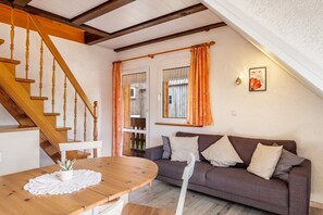 Un salon chaleureux avec un escalier en bois, un canapé agrémenté de coussins et une table à manger avec un set de table.
