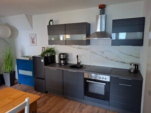 Une cuisine moderne avec des meubles de rangement aux couleurs sombres, un four encastré et une machine à café.