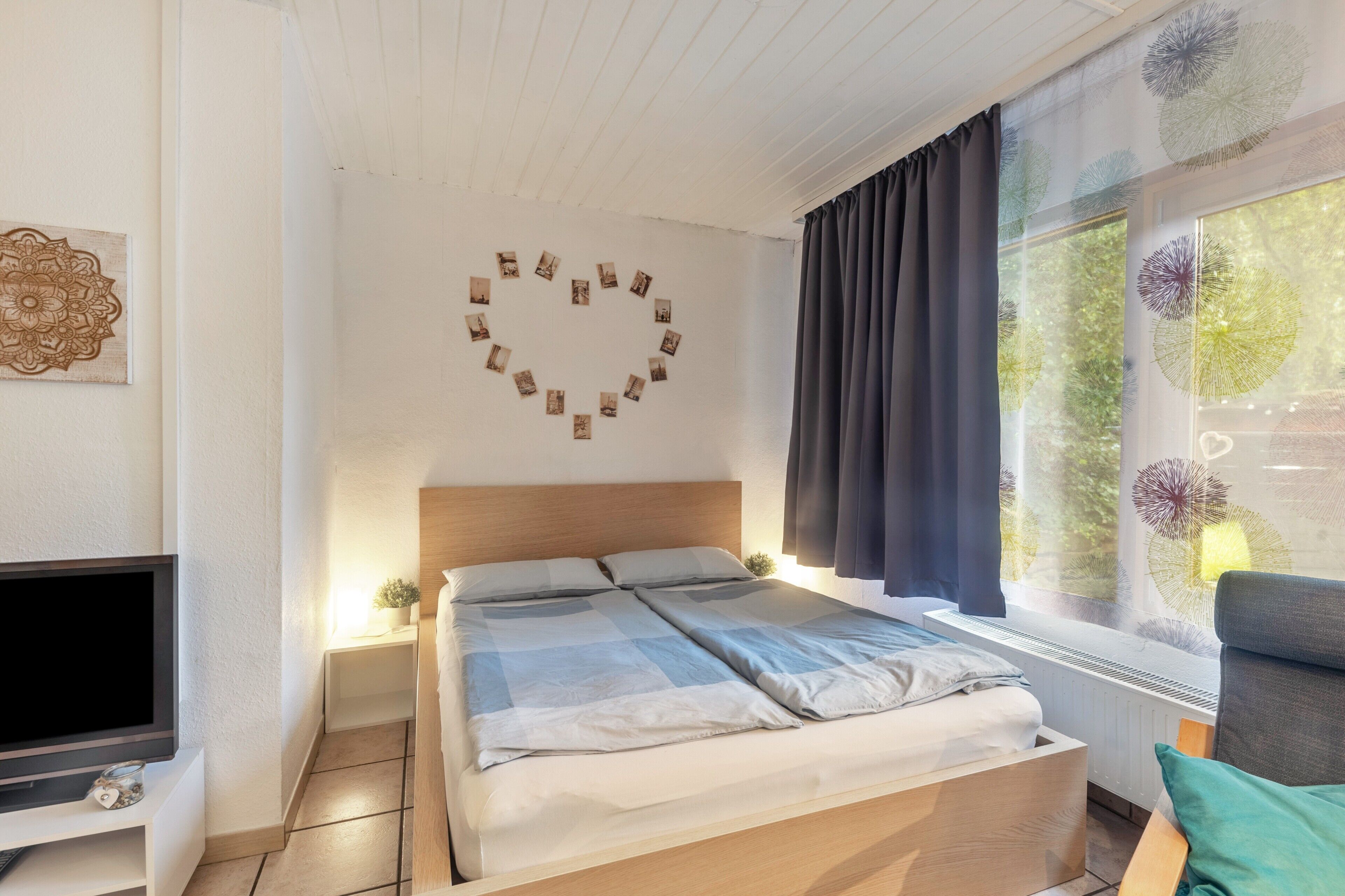Un dormitorio con una cama, televisor, decoración en la pared y una ventana con cortinas.
