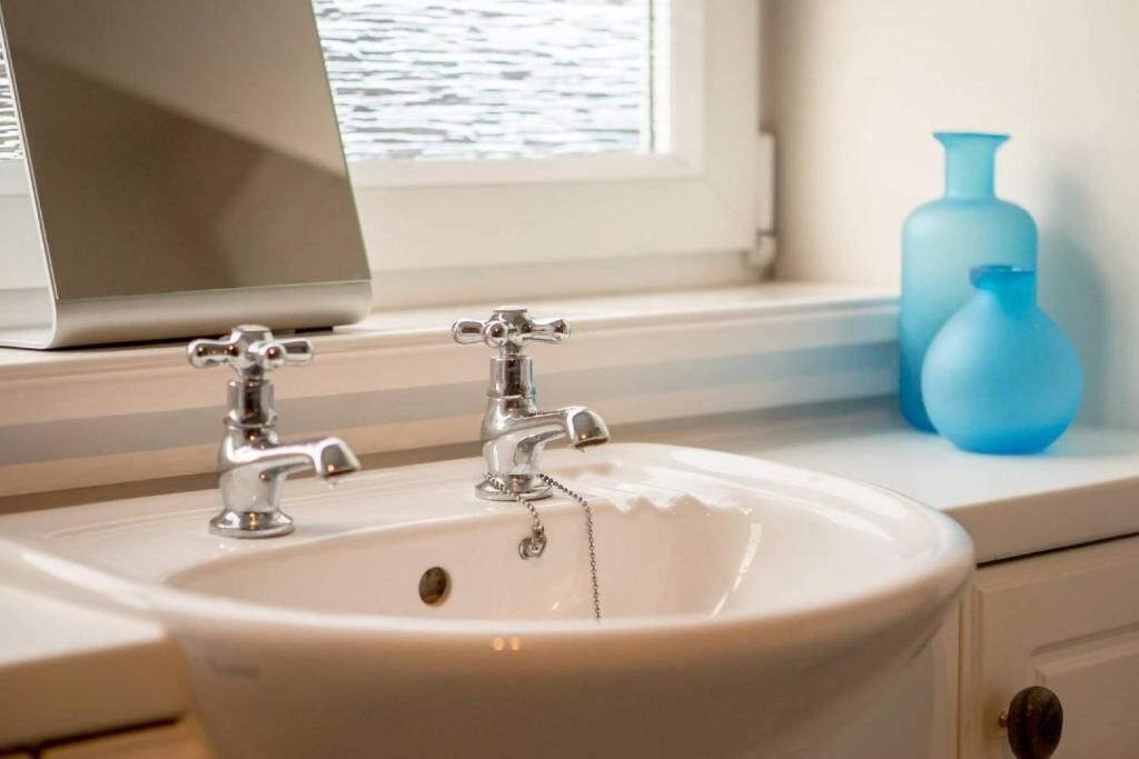 Une salle de bain avec un lavabo blanc, deux robinets et une fenêtre donnant sur l’eau.