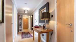 A hallway with a wooden floor, a red bowl on a table, a black lamp, and a bookshelf. - JOIVY Inviting Apartment near Leith Walk (Edinburgh)