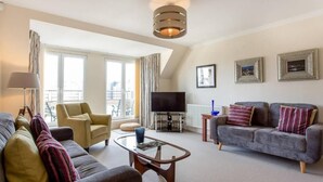 A modern living room with a sofa, armchair, and a coffee table. There is a TV and a framed picture on the wall. - JOIVY Inviting Apartment near Leith Walk (Edinburgh)